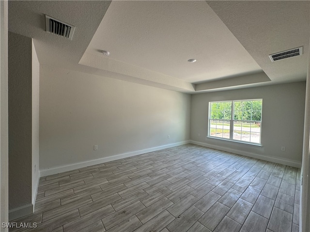 empty room with a textured ceiling, a tray ceiling, and light hardwood / wood-style floors