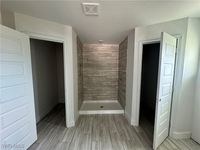 bathroom featuring hardwood / wood-style flooring, a tile shower, and a textured ceiling