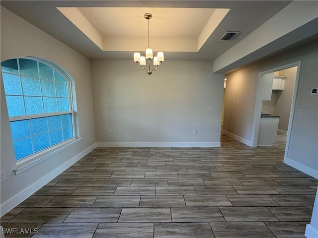 unfurnished room featuring a tray ceiling and a chandelier