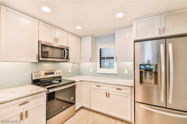 kitchen with tasteful backsplash, white cabinetry, appliances with stainless steel finishes, light wood-type flooring, and light stone counters