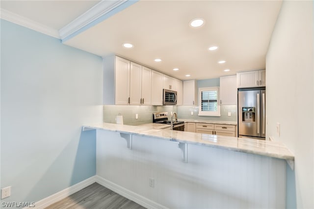 kitchen featuring kitchen peninsula, appliances with stainless steel finishes, white cabinets, light stone counters, and tasteful backsplash