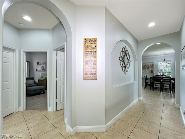 corridor featuring crown molding, light tile flooring, and a notable chandelier