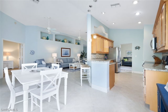 kitchen with hanging light fixtures, light tile flooring, stainless steel appliances, light stone counters, and ceiling fan