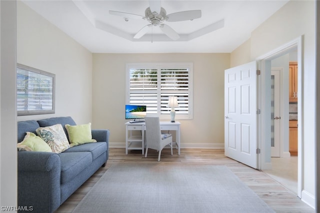 office area with ceiling fan, a tray ceiling, and light wood-type flooring