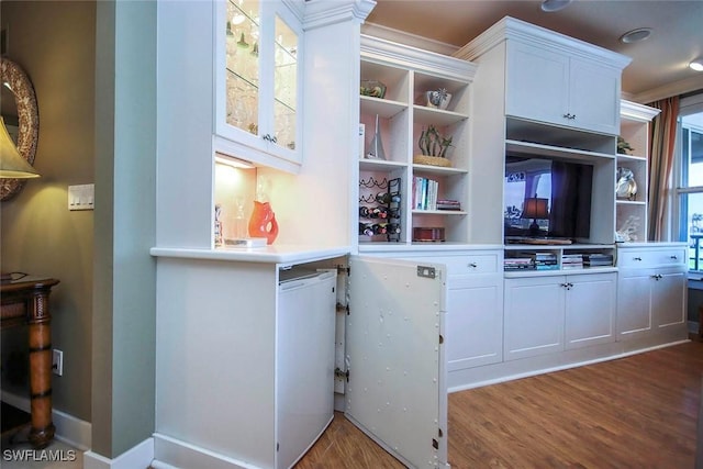 interior space featuring white cabinets, built in shelves, hardwood / wood-style flooring, and ornamental molding