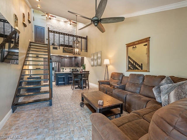 living room featuring a towering ceiling, a ceiling fan, baseboards, stairway, and crown molding