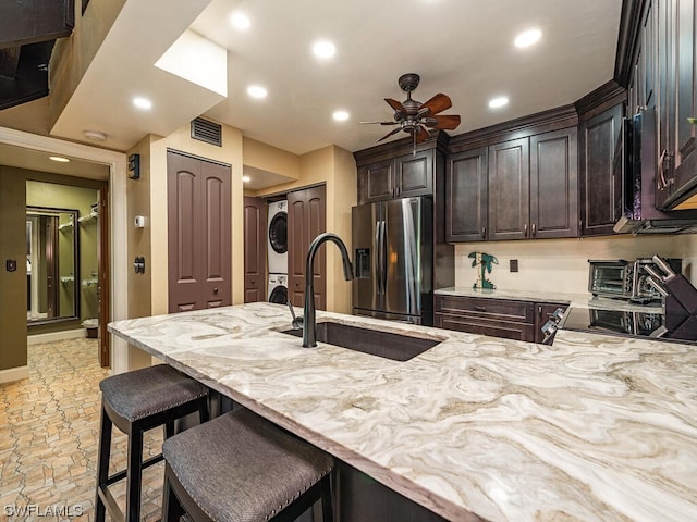 kitchen with stainless steel fridge with ice dispenser, stacked washer / drying machine, light stone counters, and ceiling fan