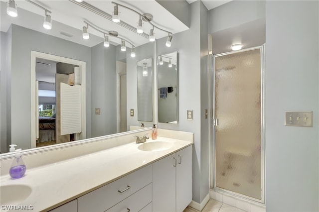 bathroom with double sink, vanity with extensive cabinet space, rail lighting, a shower with door, and tile floors