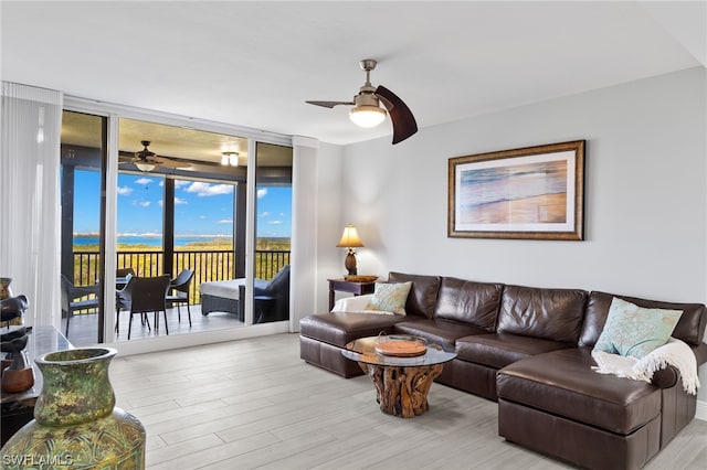 living room with a wall of windows, ceiling fan, and light wood-type flooring