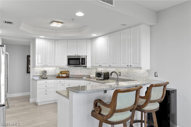 kitchen with decorative backsplash, light stone countertops, kitchen peninsula, and a raised ceiling