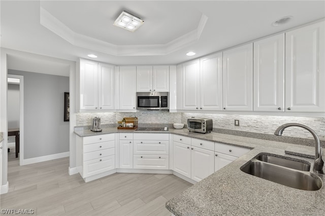 kitchen featuring white cabinetry, backsplash, light stone counters, a tray ceiling, and sink