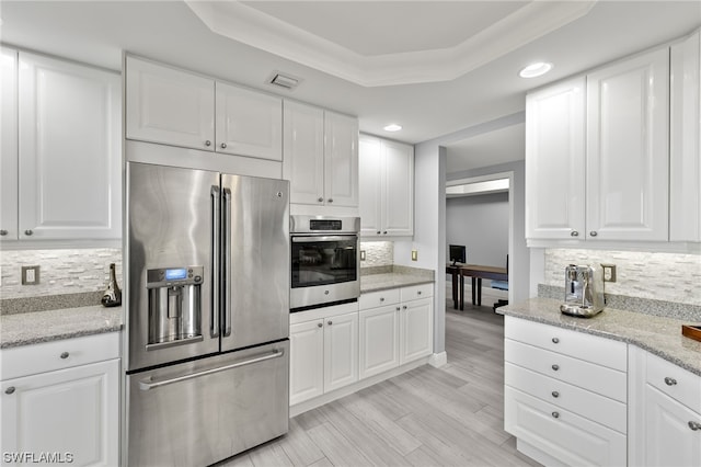 kitchen with white cabinets, backsplash, light stone counters, appliances with stainless steel finishes, and a raised ceiling