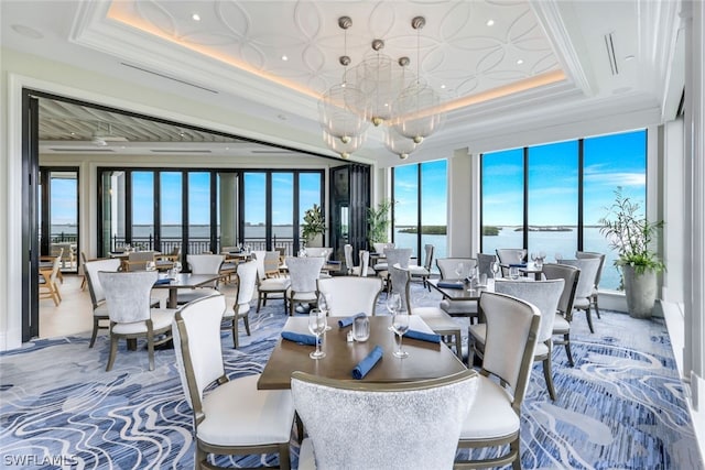 dining space featuring a raised ceiling, a water view, and a notable chandelier