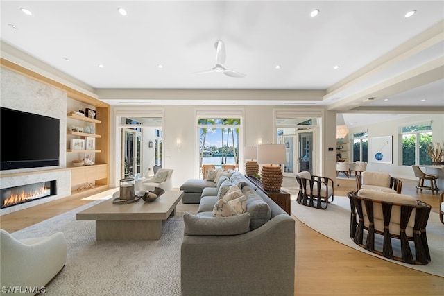 living room featuring built in shelves, ceiling fan, and light wood-type flooring