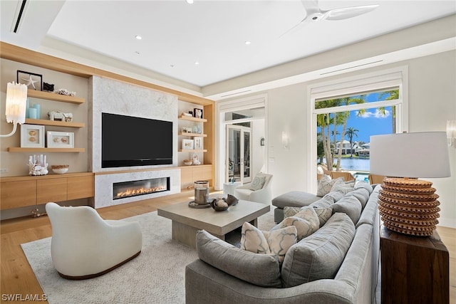 living room featuring built in features, a water view, ceiling fan, and light wood-type flooring