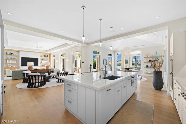 kitchen with white cabinets, light hardwood / wood-style floors, pendant lighting, and a center island with sink