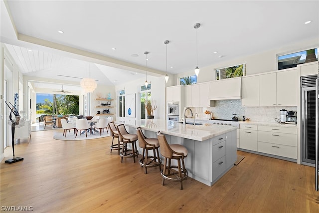 kitchen with pendant lighting, white cabinetry, a breakfast bar area, a kitchen island with sink, and light wood-type flooring