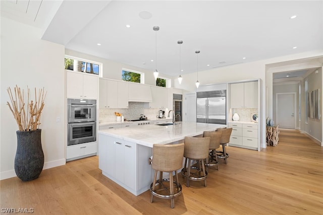 kitchen featuring white cabinets, light hardwood / wood-style floors, a kitchen island with sink, and appliances with stainless steel finishes