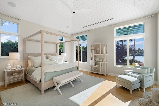 bedroom with a water view, light hardwood / wood-style floors, wooden ceiling, and multiple windows