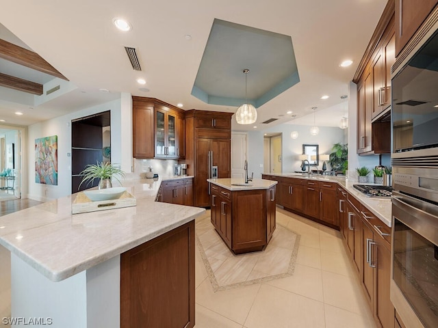 kitchen featuring a center island with sink, decorative light fixtures, paneled fridge, a raised ceiling, and kitchen peninsula