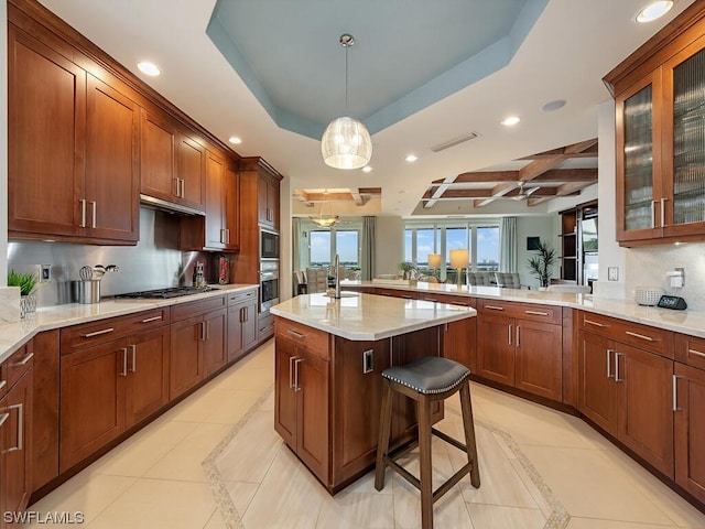 kitchen featuring stainless steel appliances, a kitchen island, a raised ceiling, hanging light fixtures, and a breakfast bar