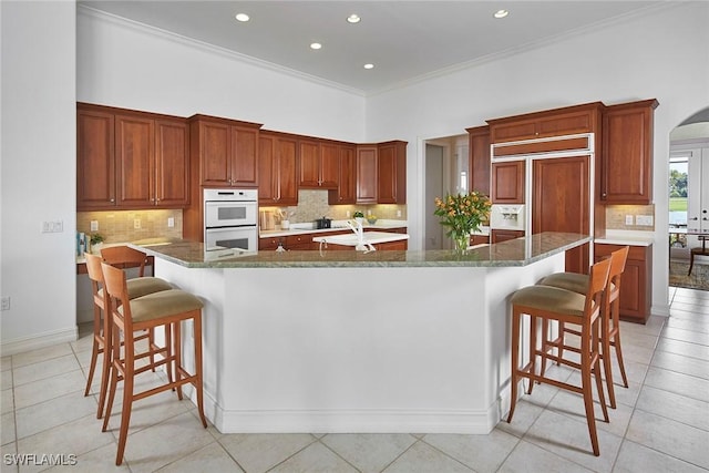 kitchen featuring double oven, arched walkways, a kitchen breakfast bar, and a large island with sink