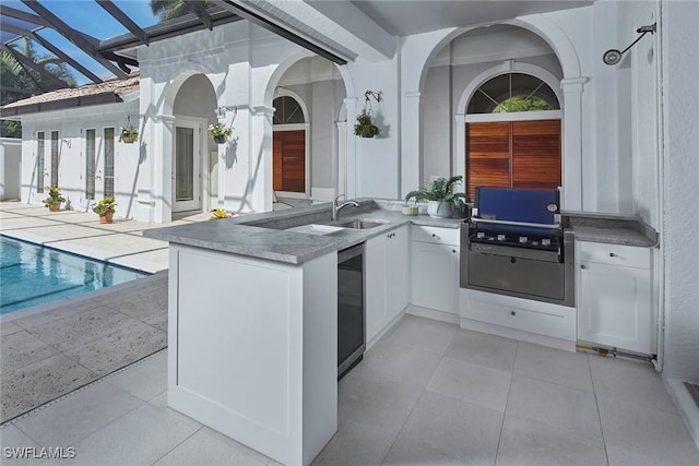 kitchen with light tile patterned floors, beverage cooler, white cabinets, light countertops, and a sink