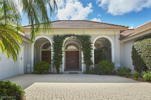 property entrance featuring a garage, decorative driveway, a tile roof, and stucco siding