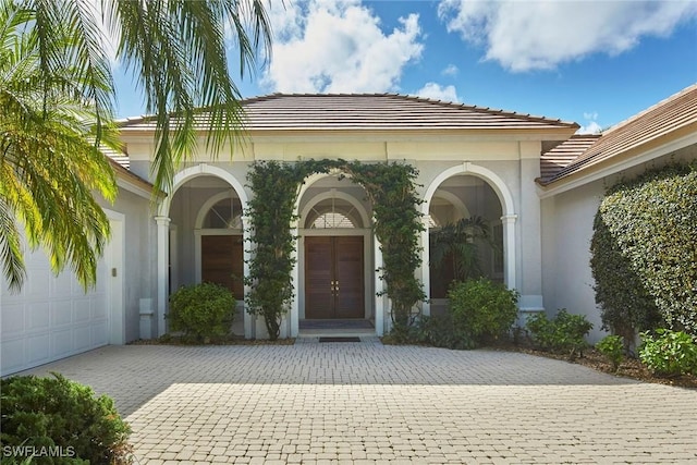 property entrance featuring an attached garage, stucco siding, a tile roof, and decorative driveway