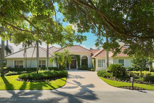 mediterranean / spanish-style home featuring a tiled roof, decorative driveway, and stucco siding