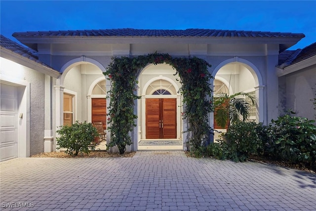 doorway to property featuring a tiled roof, decorative driveway, stucco siding, and french doors