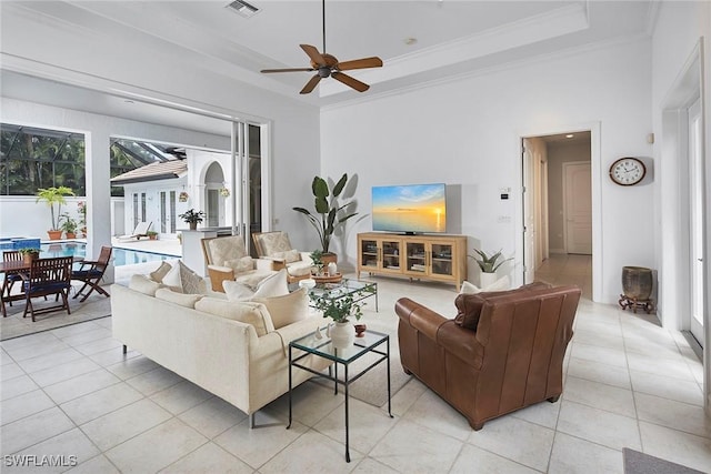 living area featuring light tile patterned floors, ornamental molding, a ceiling fan, and a tray ceiling
