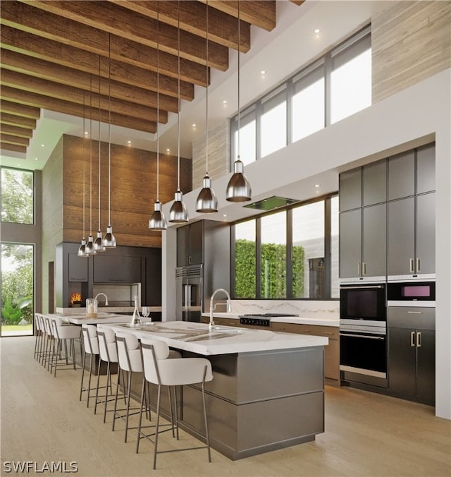 kitchen featuring a towering ceiling, gray cabinets, an island with sink, and decorative light fixtures