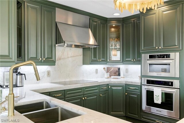 kitchen with tasteful backsplash, black electric cooktop, sink, wall chimney range hood, and green cabinets