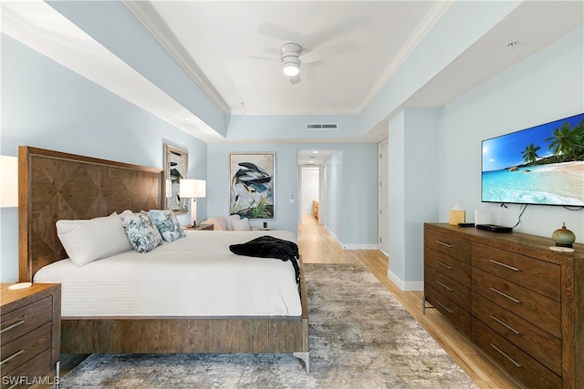 bedroom featuring visible vents, a ceiling fan, light wood-style flooring, ornamental molding, and a tray ceiling