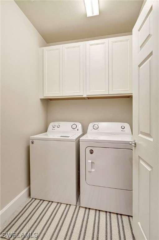 laundry room featuring washer and clothes dryer, light colored carpet, and cabinets