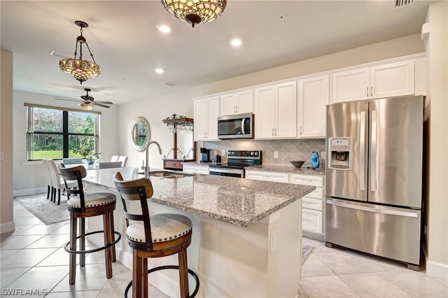 kitchen featuring an island with sink, pendant lighting, ceiling fan, appliances with stainless steel finishes, and white cabinetry