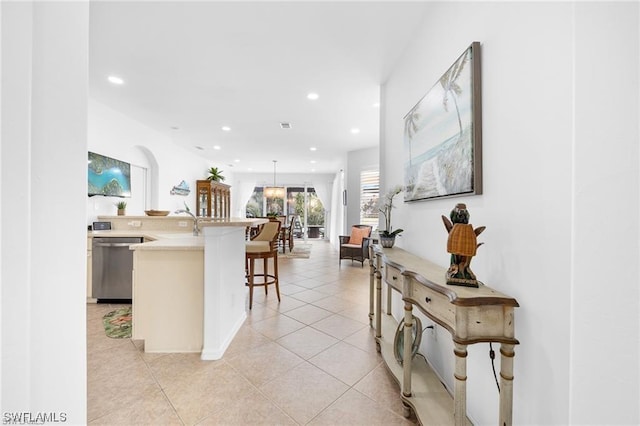 interior space with hanging light fixtures, a kitchen island, a kitchen breakfast bar, stainless steel dishwasher, and light tile patterned floors