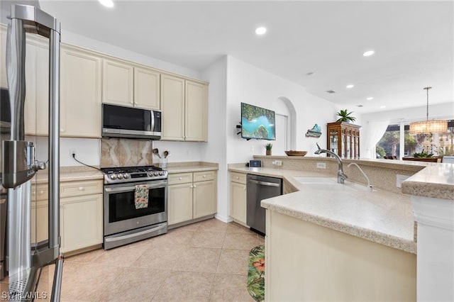 kitchen with sink, hanging light fixtures, cream cabinets, light tile patterned floors, and appliances with stainless steel finishes