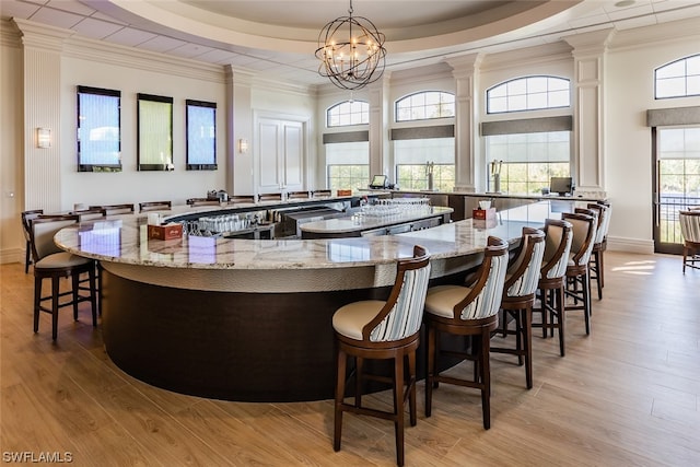 bar with decorative light fixtures, a tray ceiling, light stone counters, and light hardwood / wood-style flooring