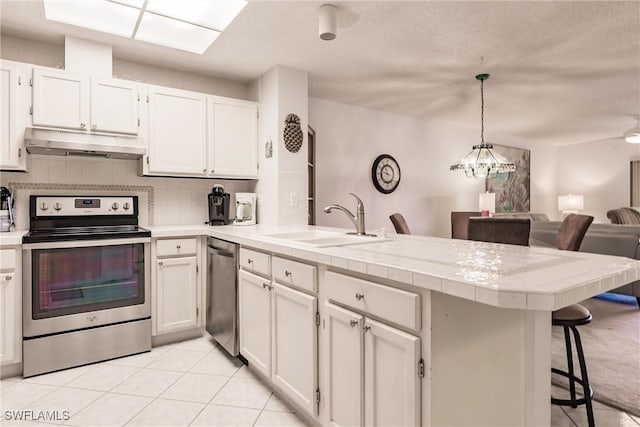 kitchen with under cabinet range hood, a peninsula, a sink, appliances with stainless steel finishes, and decorative backsplash