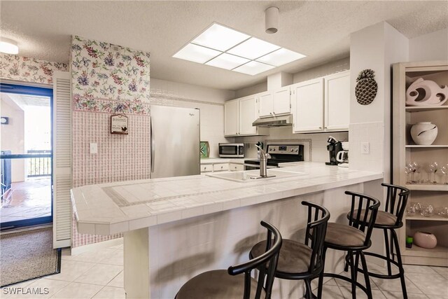 kitchen with tile countertops, a breakfast bar area, stainless steel appliances, a peninsula, and under cabinet range hood