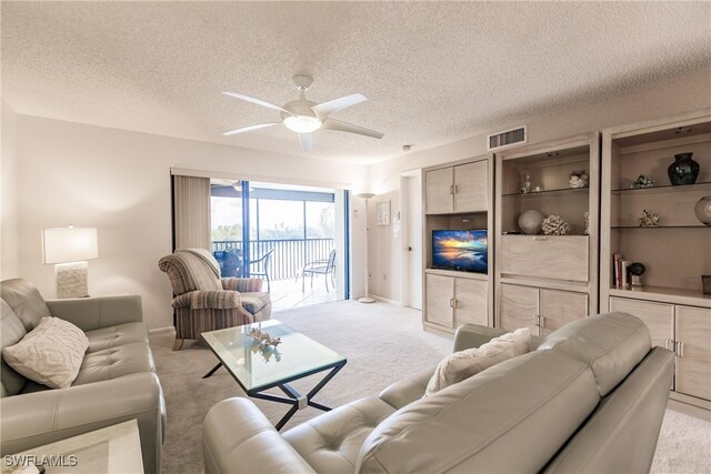 living area featuring a textured ceiling, ceiling fan, visible vents, and light colored carpet