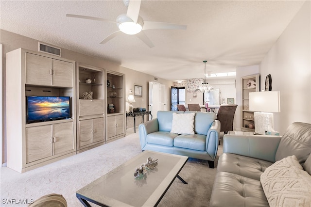 living area featuring light carpet, a textured ceiling, ceiling fan with notable chandelier, and visible vents