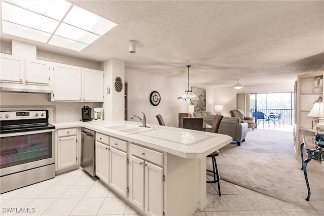 kitchen featuring light carpet, appliances with stainless steel finishes, a peninsula, under cabinet range hood, and a sink