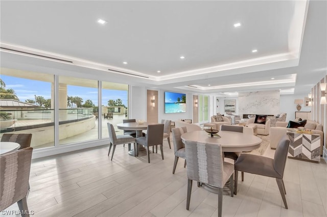 dining space with a raised ceiling, a large fireplace, and light hardwood / wood-style flooring