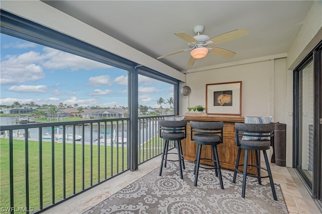 balcony featuring an outdoor bar, a water view, and ceiling fan