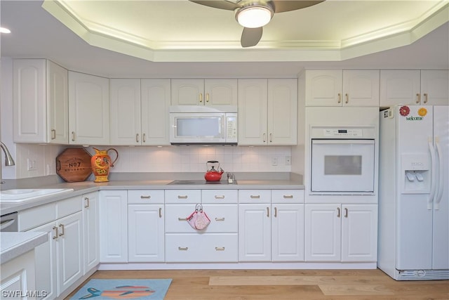 kitchen with white appliances, sink, light wood-type flooring, white cabinetry, and a tray ceiling