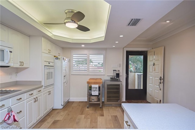 kitchen with white appliances, a tray ceiling, wine cooler, crown molding, and white cabinets