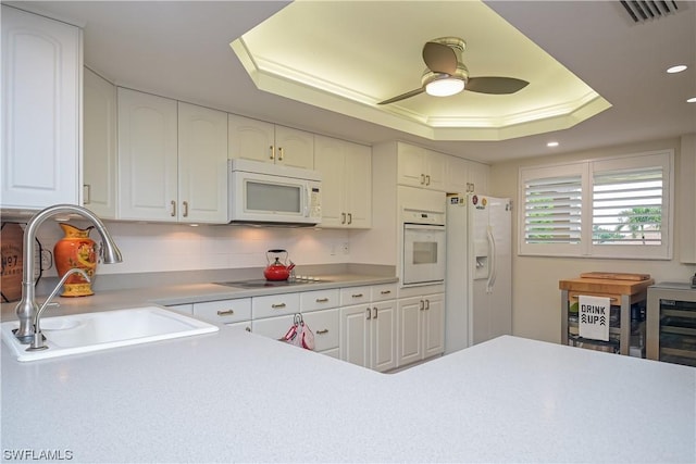 kitchen with a tray ceiling, white appliances, sink, and white cabinetry